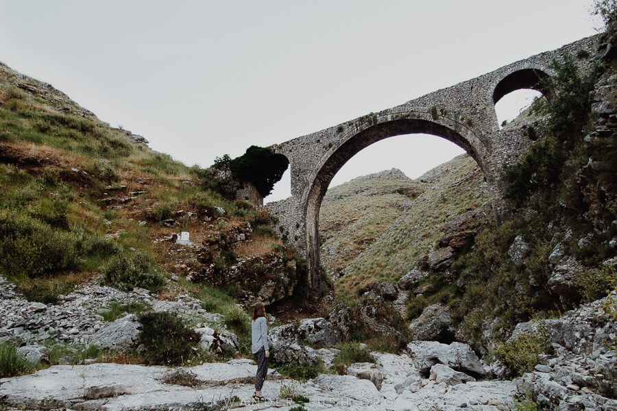 A woman looking up at an arched stone bridge.