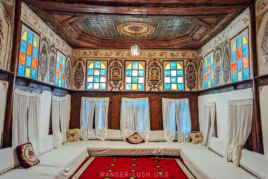 A sitting room inside Zekate House, an Ottoman mansion in Gjirokaster, with painted walls and carpets on the floor.