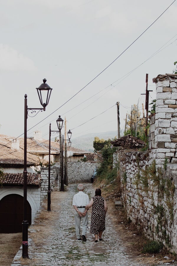 An elderley couple walking down a stone street.