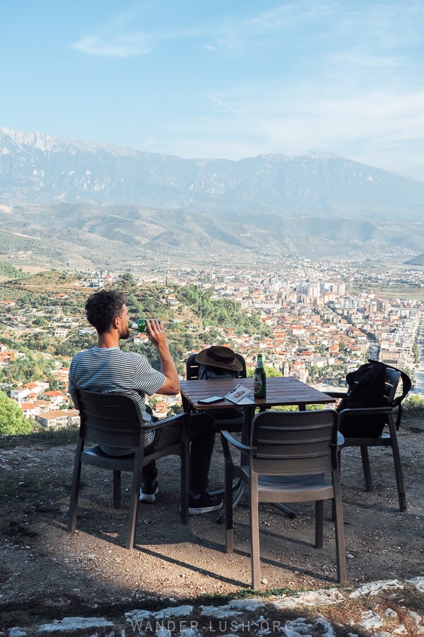 A man seated at a plastic table drinking from a bottle of beer at a restaurant in Berat, Albania.