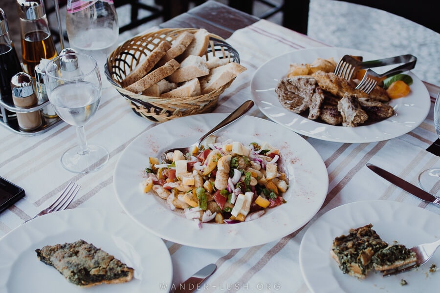 A table set with salad, meat, bread and wine glasses. Eating local cuisine is one of the best things to do in Berat, Albania.