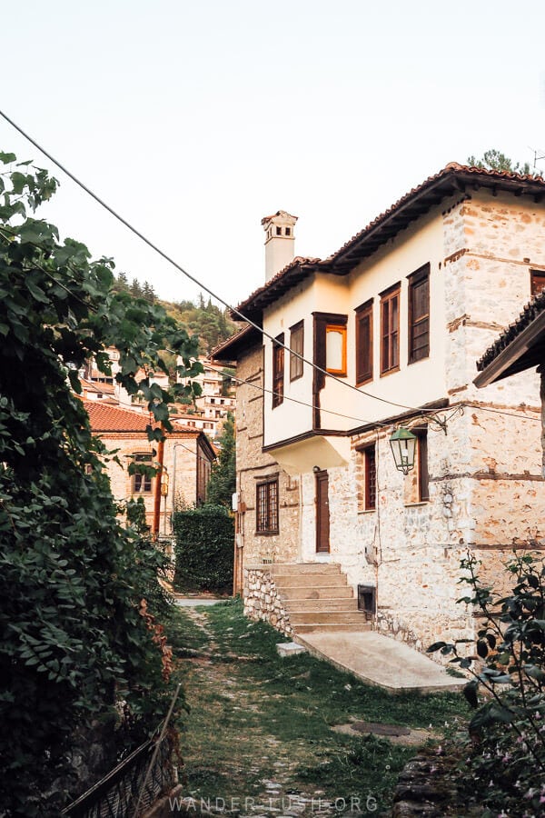 An ancient Ottoman house in Kastoria, Greece, viewed down a leafy alleyway in a historic neighbourhood.