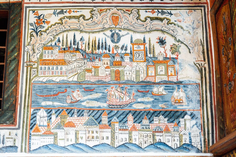 A fresco of a city scene with sail boats in the foreground painted in blue and red tones, as seen inside the restored Tsiatsiapas Mansion in Kastoria.