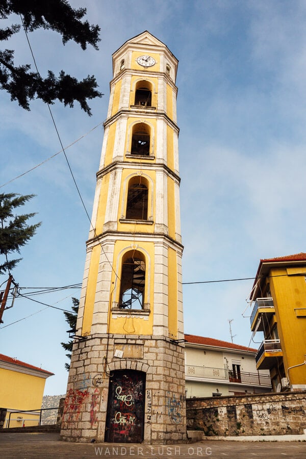 The bell tower in Kastoria, a tall 19-metre bell tower painted lemon yellow against a blue sky.