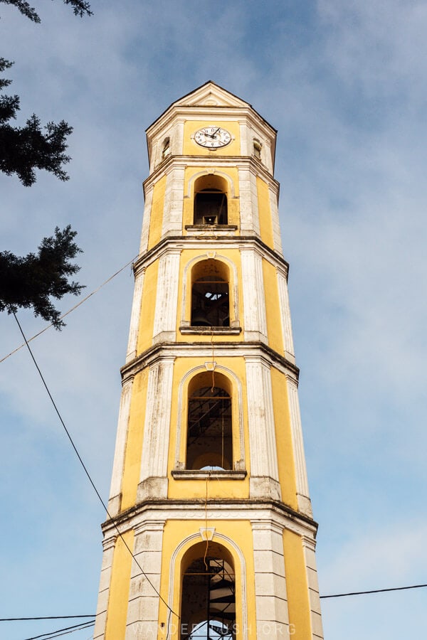 The bell tower in Kastoria, a tall 19-metre bell tower painted lemon yellow against a blue sky.