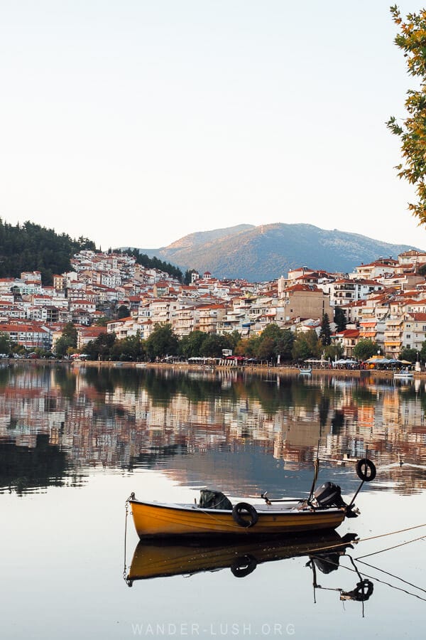 A small fishing boat floating in a harbour in front of houses in Kastoria, Greece.