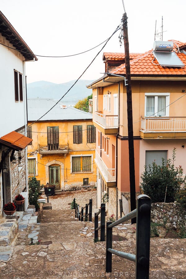 A view of the lake from an alleyway in Kastoria, framed by pink and yellow houses.