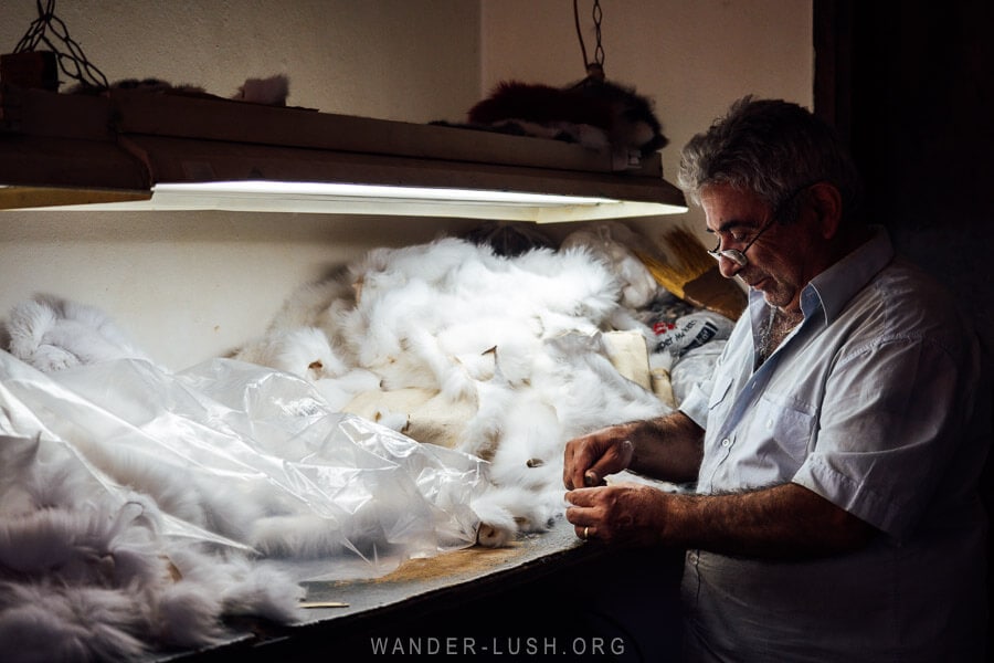 A man behind a workbench sewing animal fur in his studio in Kastoria.