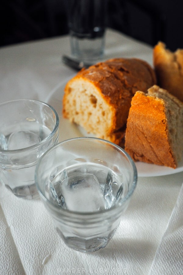 Two glasses of tsipouro Greek alcohol on a white tablecloth with crusty bread in the background.