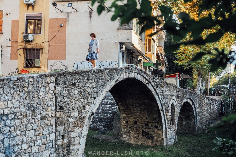 A woman walks across the Tanner's Bridge in Tirana, an ancient stone bridge with a half-moon shape.