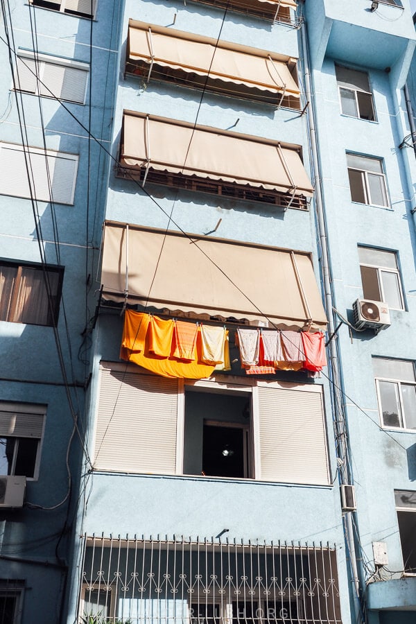 A blue apartment building in Tirana with colourful laundry hanging out front.