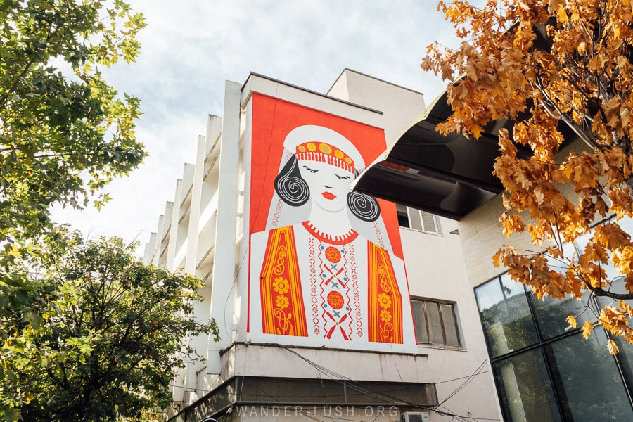Mural of a woman dressed in traditional clothing on the side of an office building in Tirana, Albania.