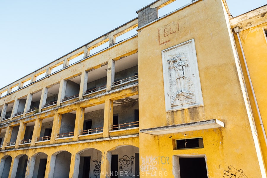 An abandoned hotel painted canary yellow with old frieze sculptures in the mountains above Tirana.