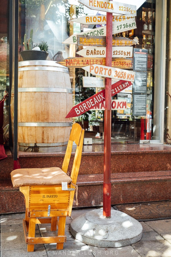 A sign in front of a wine shop in Tirana with arrows pointing to different wine regions around the world.