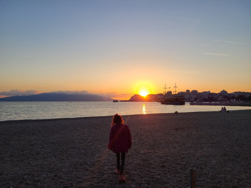 a girl walks down the beach in Saranda Albania towards the sunset in the first month of our family gap year.