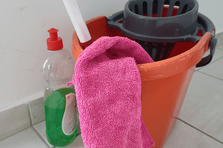 A bucket with a mop and other cleaning supplies