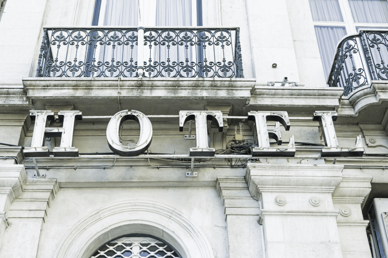 A historical building with ornate juliette balcony above a vintage light up sign that reads hotel