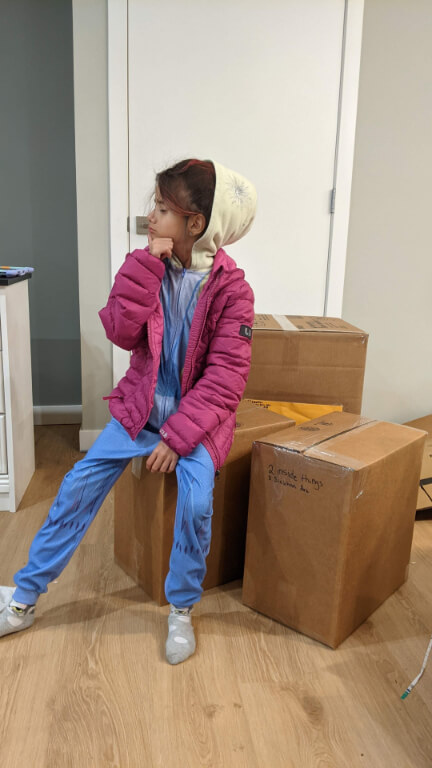 A young girl sits on one of three cardboard boxes pondering life