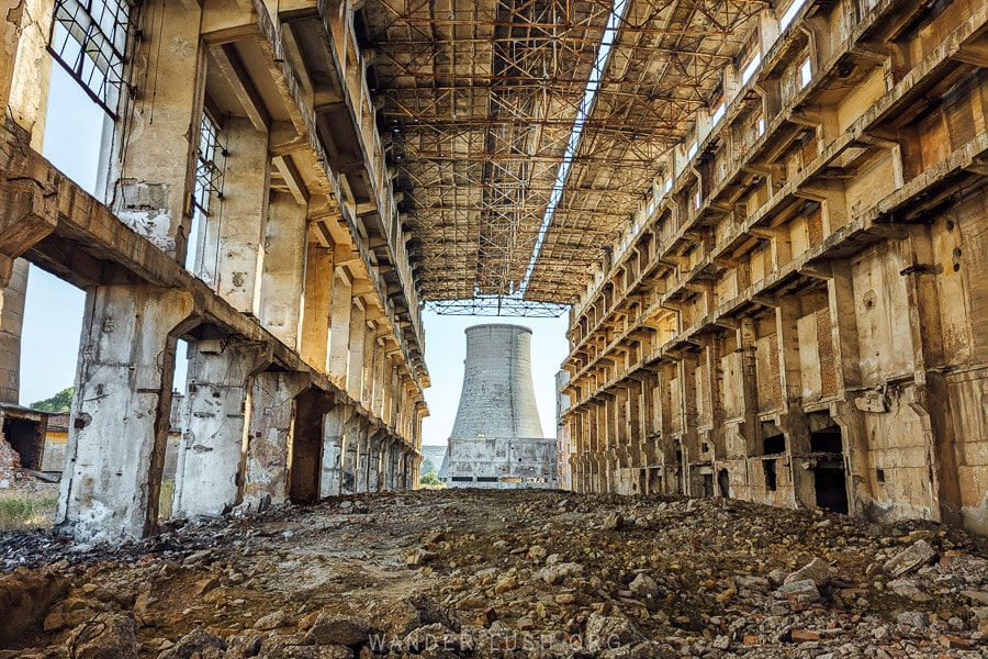 The abandoned Fier power station, with a cooling tower viewed from inside a ruined concrete building.
