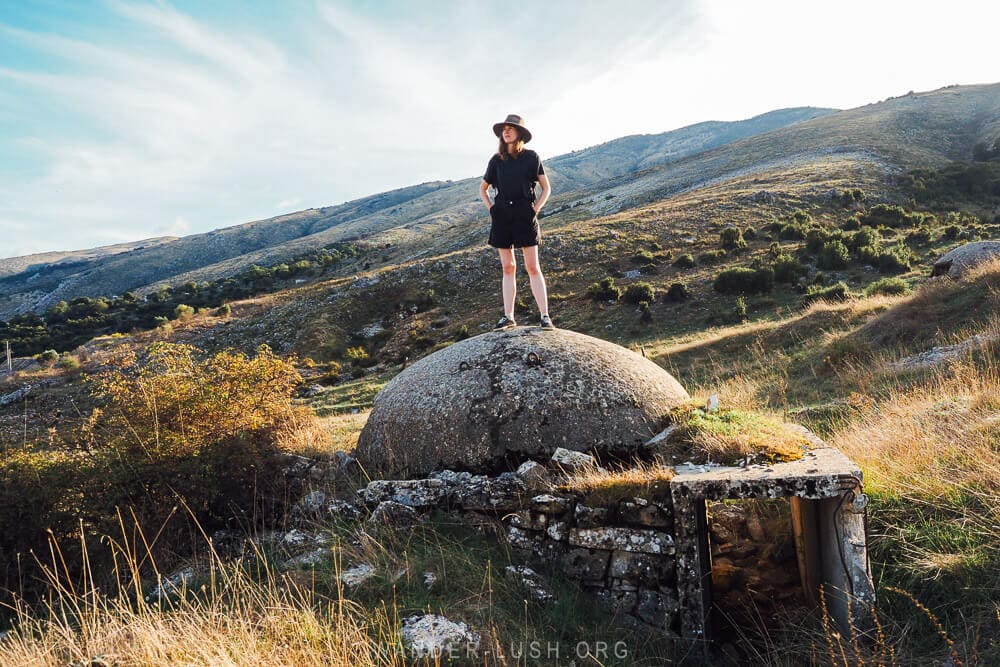 A woman standing on a concrete bunker in a field near Gjirokaster in Albania.