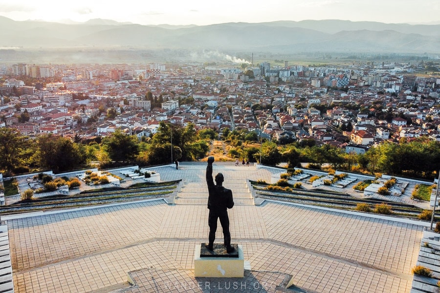 View of Korca city at sunset with the WWII statue, a man raising his fist, in the foreground.