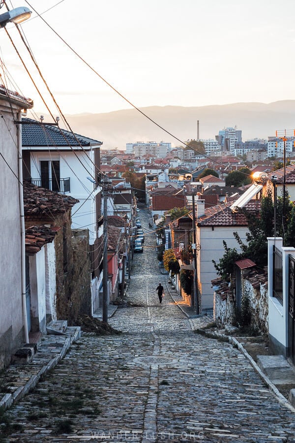 A cobbled old street in Korca leads down to rows of houses.