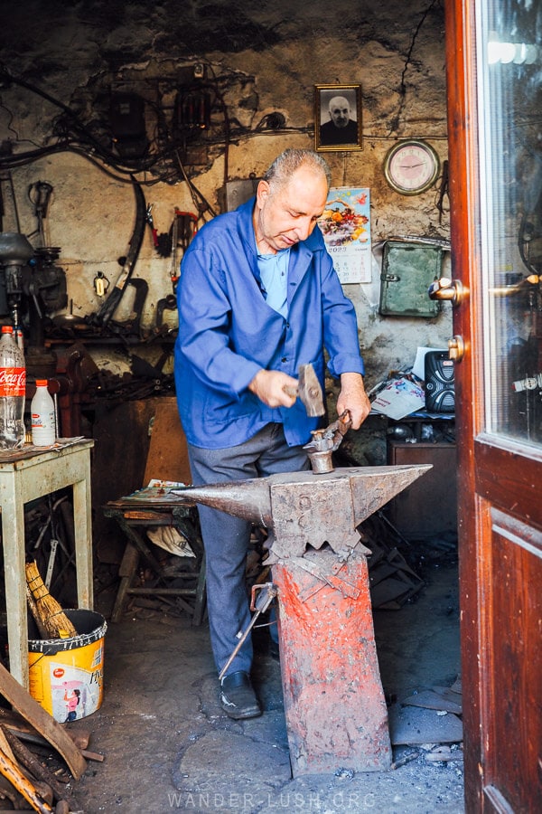 A craftsman inside the Korca bazaar hitting an object on an anvil.