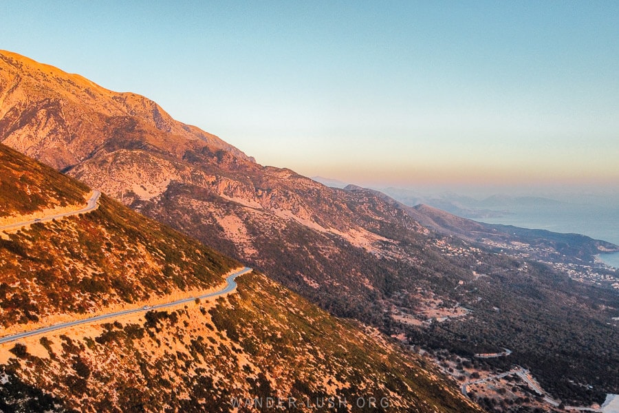 The Llogara Pass road winds its way down mountains in Albania towards the sea at sunset.