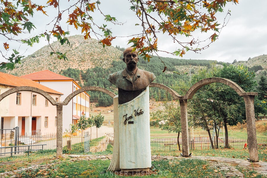 A statue in the town of Leskovik, Albania depicting a local hero, with concrete arches behind him.