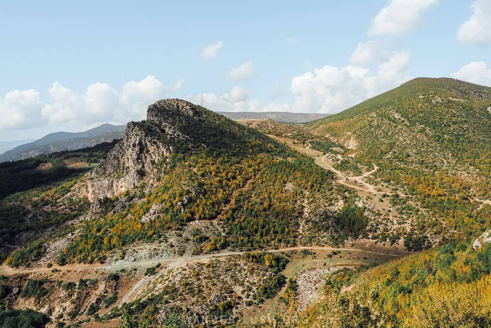 Green mountains and a limestone peak wrapped in a dirt road outside Leskovik in Albania.