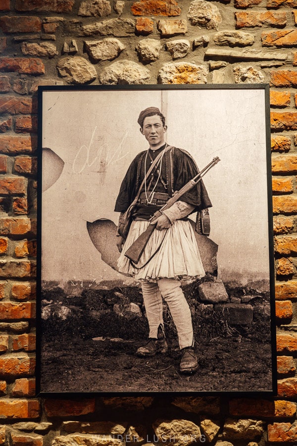 An archival photo of a man in traditional Albanian dress hanging on a brick wall inside the Leskovik Melesin Distillery.