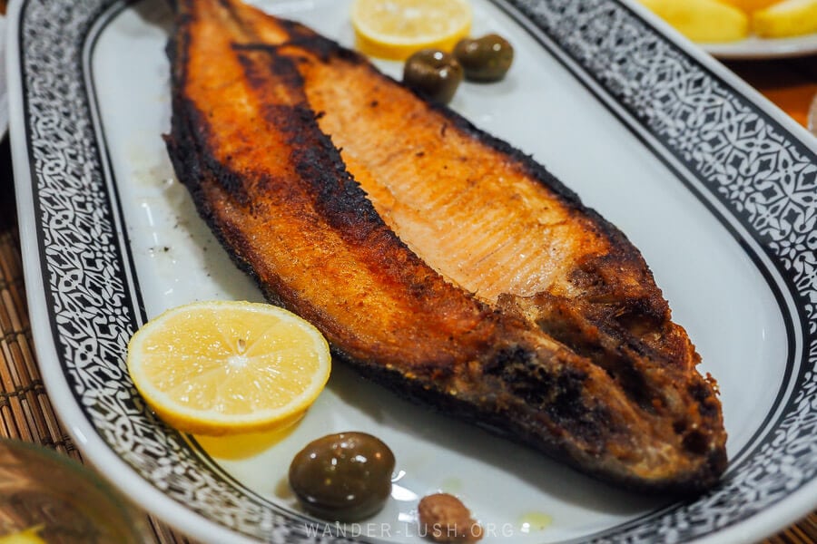 A piece of chargrilled fish accompanied by lemon and olives on a plate at a guesthouse in Lin, Albania.