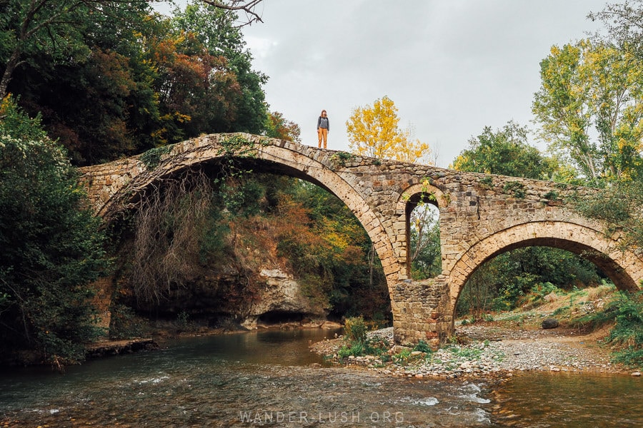 A woman stands atop the arch of an Ottoman stone bridge in Albania known as the Golikut Bridge.