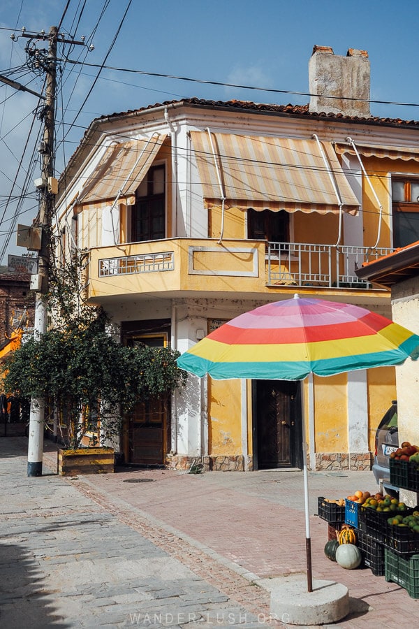 A heritage yellow corner building in Pogradec, Albania with a rainbow umbrella and market stall.