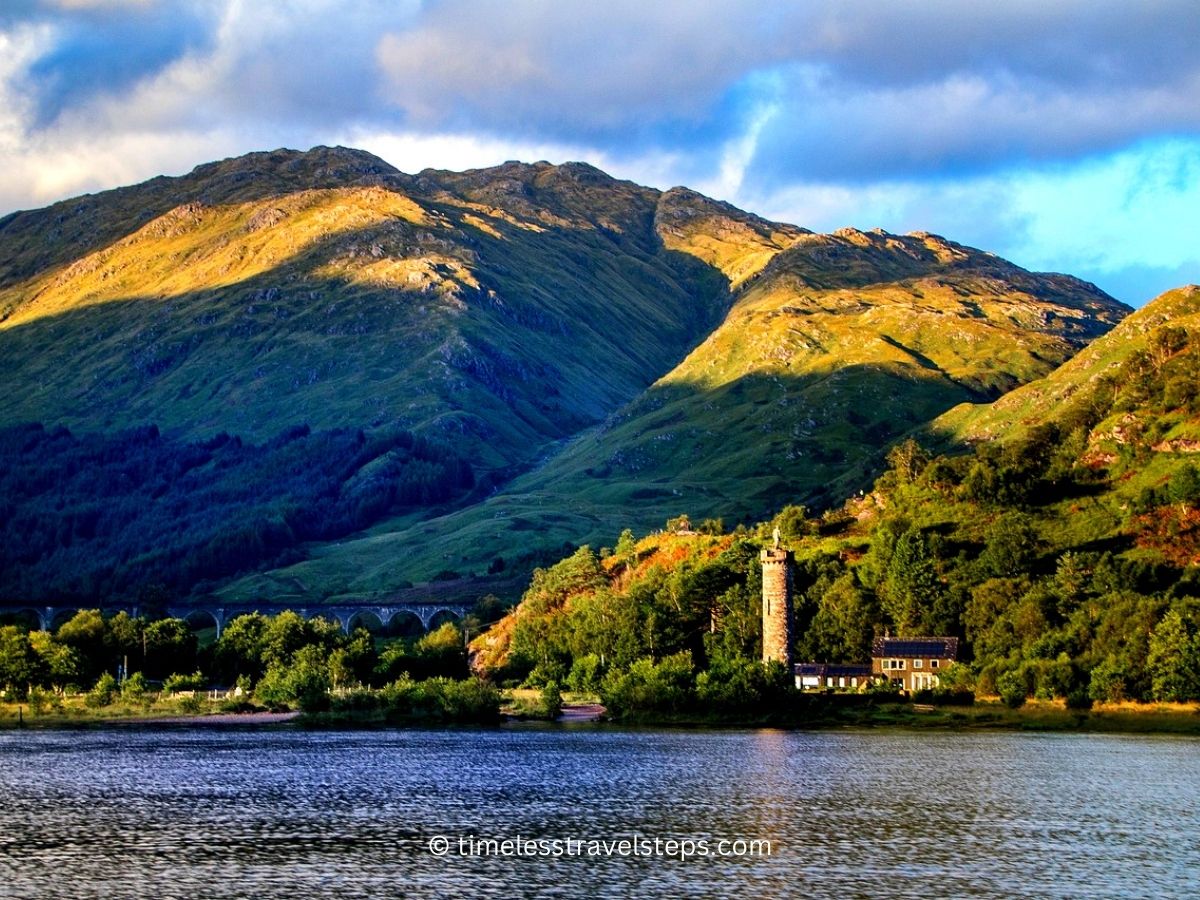 Glenfinnan monument viewed from the waters of loch shiel with the sun casting a shadow on the mountains