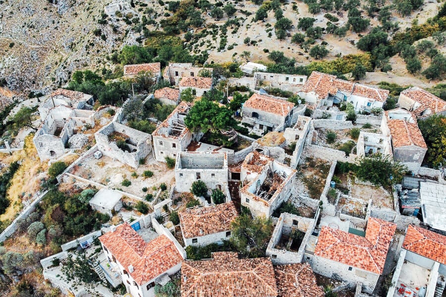 An aerial view of old stone houses in an abandoned Albanian village, with only their foundations visible.