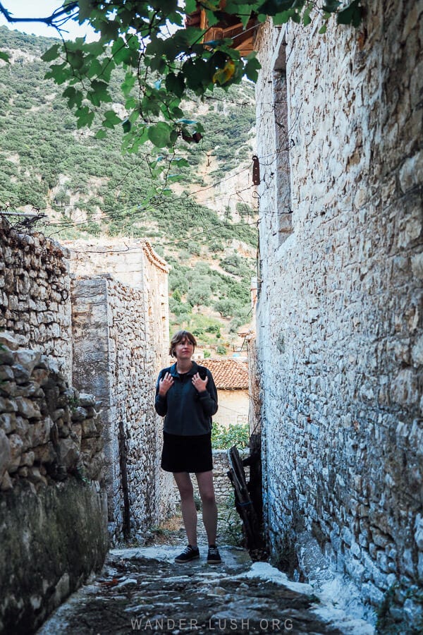 A woman wearing a backpack walks down a narrow cobbled alleyway in Qeparo village in Albania.