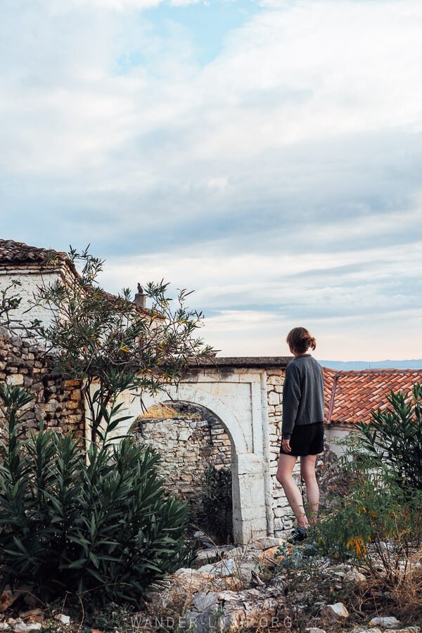 A woman in a grey jumper looking out to heritage buildings in old Qeparo village in Albania.