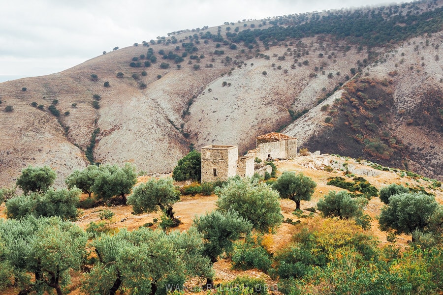 Ali Pasha Castle, a stone fortress behind olive trees at the foot of grey and purple mountains on the Albanian Riviera.