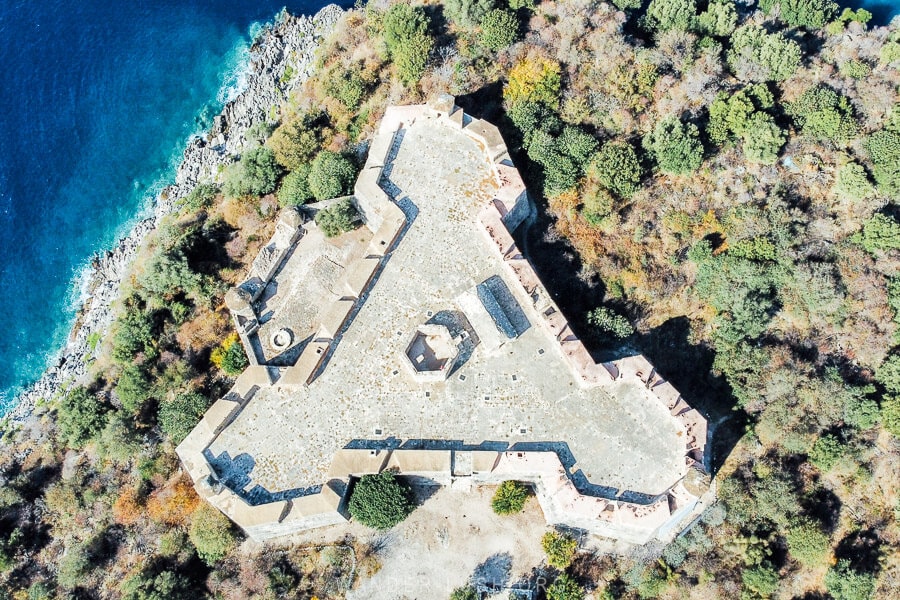 A drone photo of Porta Palermo castle, a triangle-shaped castle on a peninsula in Albania with the sea on one side.