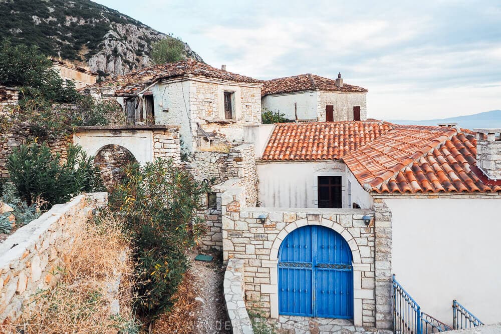 A royal blue gateway on a restored stone building in Qeparo village, with the outline of mountains in the distance.