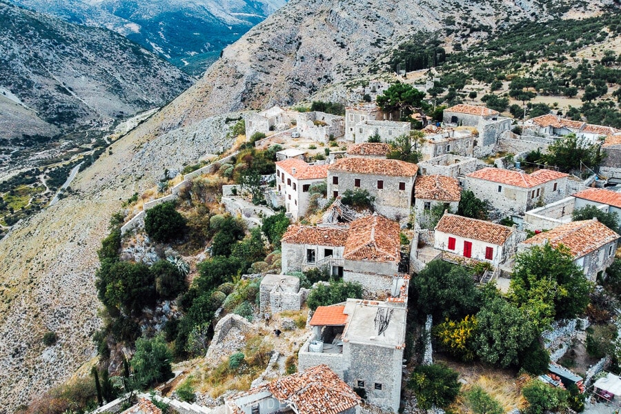 Houses on a mountainside in Upper Qeparo, with a river valley and blue hills stretching out into the distance.