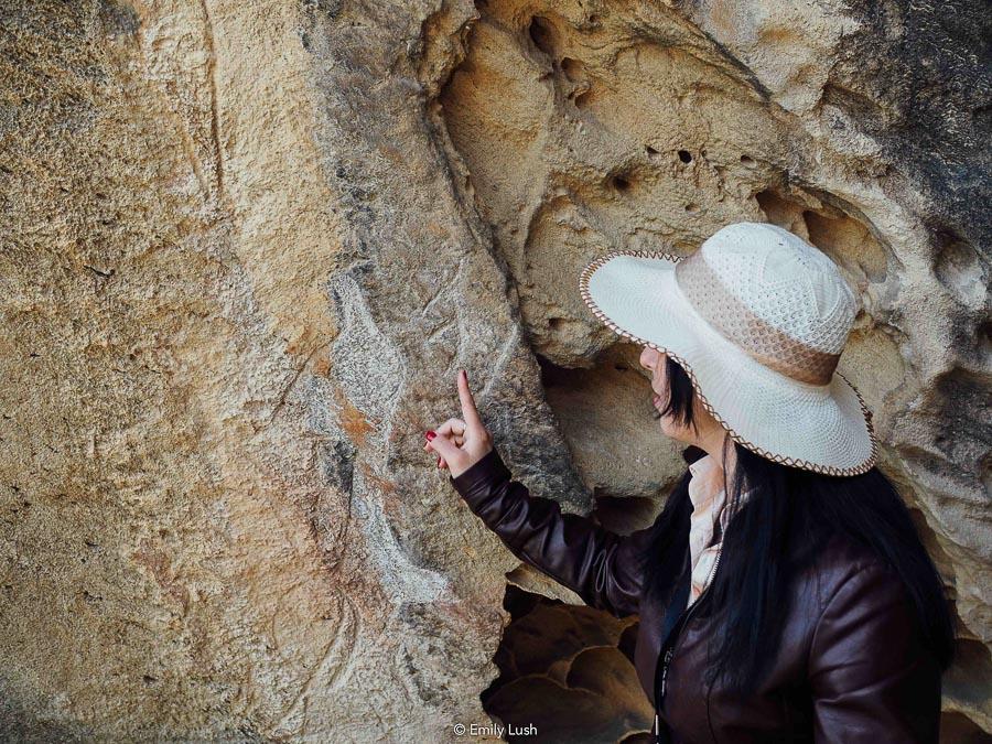 A woman points to a petroglyph on a rock wall in Gobustan, Azerbaijan.