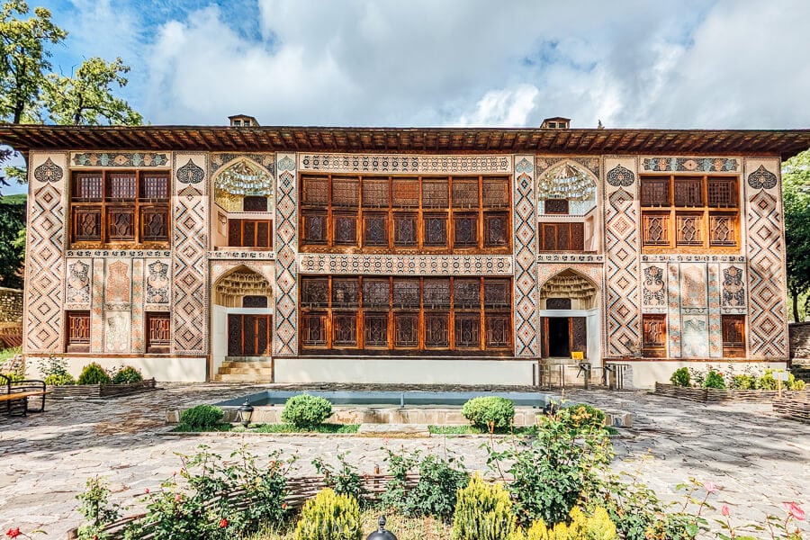 The Palace of the Sheki Khans, an 18th century palace in Sheki, Azerbaijan, its front facade decorated with mirrors and stucco and a rose garden out front.