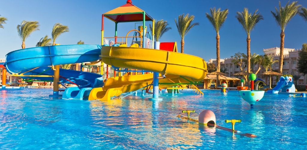 A yellow and blue swirl slide in the center of the pool, as well as trees surrounding the pool's perimeter. 
