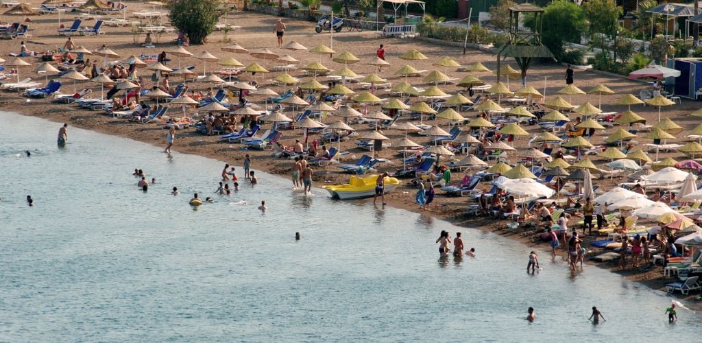 A beach front and a lot of beach small tents  on the shore and a crowded people enjoying the beach. 