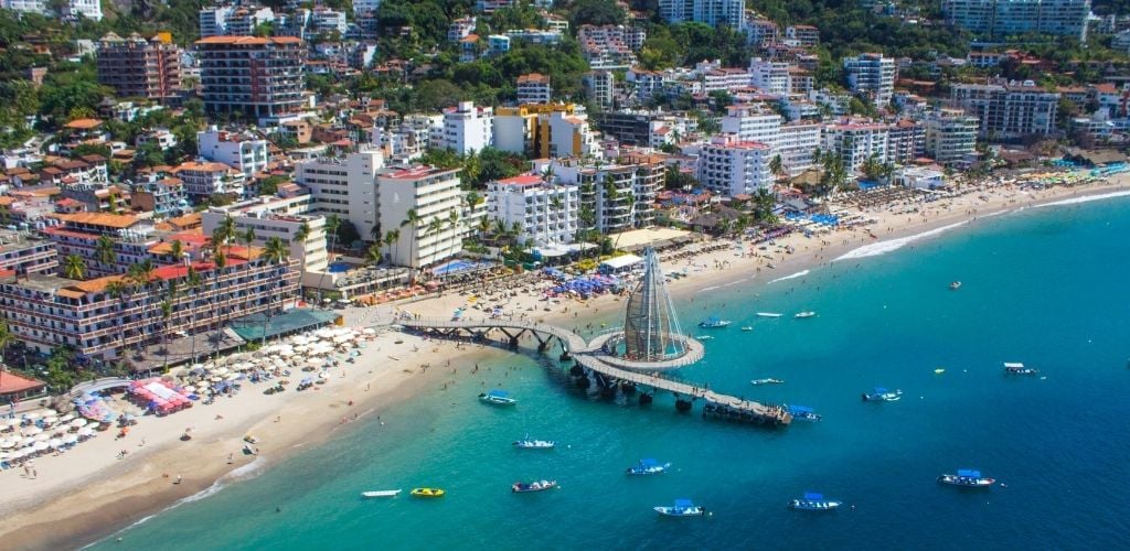 Puerto Vallarta bay from the air. lots of buildings and people on the shore and a path way going to sea, a few floating boat. 