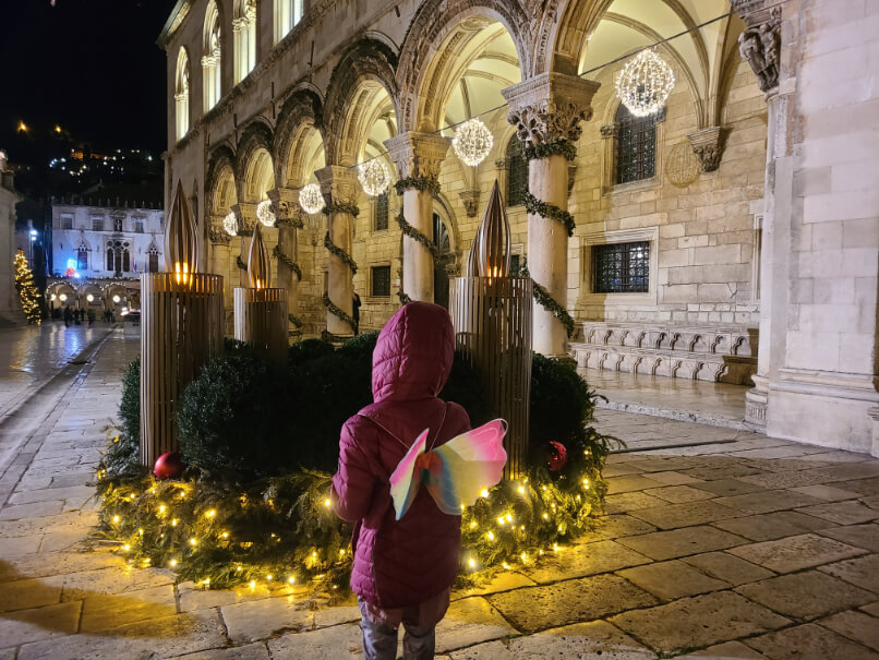 Girl wears fairy wings in front of the advent wreath at Rector's Palace in Dubrovnik in December at Christmas Time