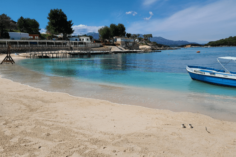 A blue boat floats by on the turquoise waters of Ksamil Beach - Plazhi i Ksamilit Albania