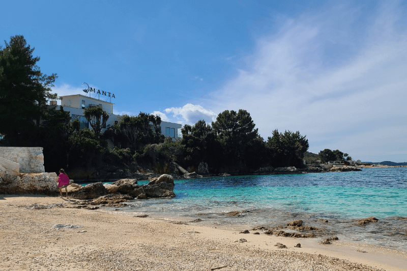 Trees and rocks line the far shoreline of the turquoise waters of Coco Beach in Ksamil Albania